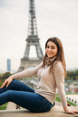 Fototapeta premium Beautiful girl posing to the photographer against the background of the Eiffel Tower. Autumn photosession. Sunny weather. Beautiful smile and makeup