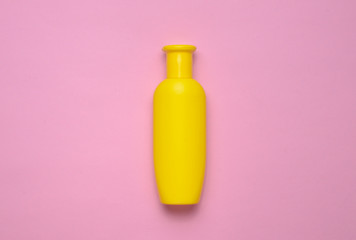 Yellow bottle of shampoo on a pink pastel background. Trend of minimalism. Top view. Products for the shower. Space for text.