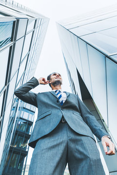 businessman with earphones stands between skyscrapers