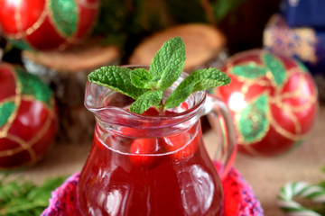 Hot cranberry tea in a glass jug surrounded by Christmas attributes