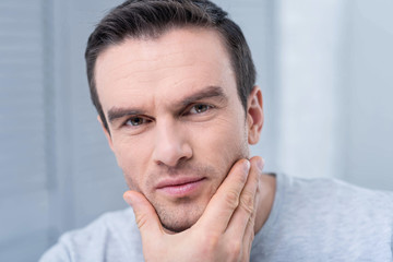 Morning procedures. Attractive young focused man looking at the camera posing on the light background after shaving