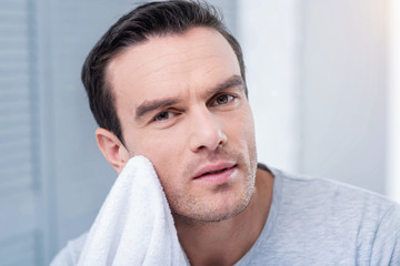 Fototapeta premium Work time. Pleasant attractive man putting white towel against the chin looking straight while posing on the light background