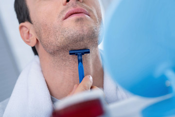 Accurate work. Close up of blue modern daily razor hold by man hands while he shaving his neck and standing in front of mirror