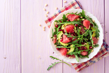 Fresh salad with arugula, grapefruit, avocado, pomegranate seeds and pine nuts.