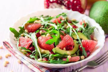 Fresh salad with arugula, grapefruit, avocado, pomegranate seeds and pine nuts.
