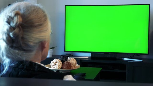 Old caucasian woman watches television in living room - green screen - closeup