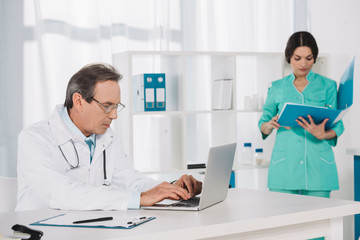 Fototapeta na wymiar nurse searching something in folder and doctor using laptop