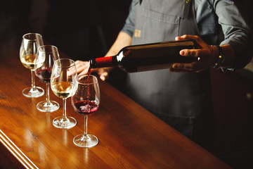 Bartender pours red wine in glasses on wooden bar counter