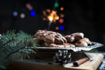 gingerbread cookies for the new year on a silver tray, New Year's lights, fireworks, fur-tree, cones, cinnamon on a wooden cutting board on a dark background