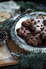 gingerbread cookies for the new year and Christmas on a silver tray, Christmas tree, cones, cinnamon on a wooden cutting board on a dark background