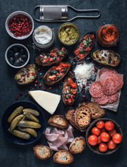 Served bruschettas on the table with ingredients for preparing on dark background