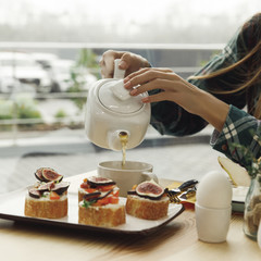 cropped shot of girl pouring tea from teapot while having breakfast