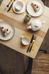top view of teapot, empty cups and gourmet pastries on plates on wooden table