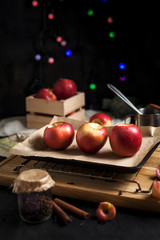 cooking of baked apples for New Year's holidays, Christmas tree and New Year's lights, honey and cinnamon on a wooden cutting board on a dark background