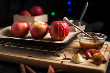 cooking of baked apples for New Year's holidays, Christmas tree and New Year's lights, honey and cinnamon on a wooden cutting board on a dark background