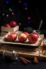 cooking of baked apples for New Year's holidays, Christmas tree and New Year's lights, honey and cinnamon on a wooden cutting board on a dark background