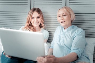 Fototapeta premium Mother and daughter. Positive nice cheerful women looking at the laptop screen and smiling while sitting together