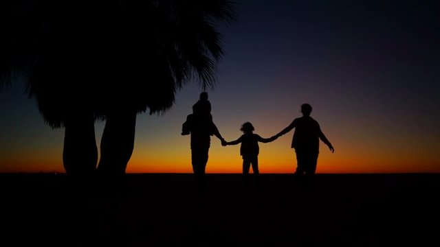 Mom, father and two children are walking along the beach. Silhouettes of the family against the setting sun. Romantic weekend