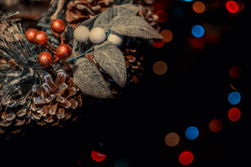 A Christmas wreath made of cones and needles in the corner and blurred multicolored lights on a dark background. Festive background, screensaver.
