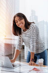 Modern office. Pretty female person keeping smile on her face and standing at her workplace while using laptop