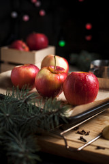 cooking of baked apples for New Year's holidays, Christmas tree and New Year's lights, honey and cinnamon on a wooden cutting board on a dark background