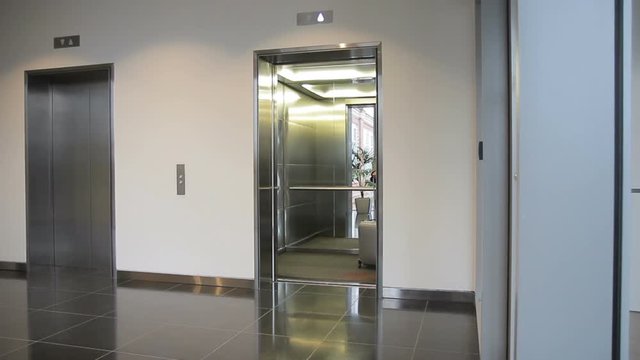 The blond businesswoman is going to the elevator in luxury hotel during the trip. The lady in warm gray jacket and with lugage bag waits for the lift in the big empty hall to get up to her room