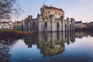Fototapeta na wymiar Gravensteen - historical medieval castle on water in Ghent, Flanders, Belgium. Castle of Counts stronghold reflected on canal in Gent city by sunset.