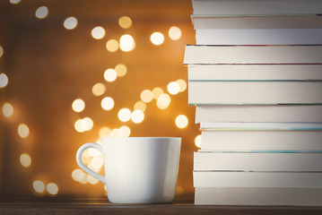 White cup of hot drink near pile of books and fairy lights