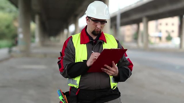 Worker makes notes in his works documentation. Building inspector with work documentation at project site