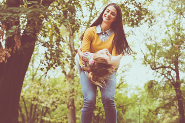 Mother holding daughter in arms and spinning around. Playing in nature.