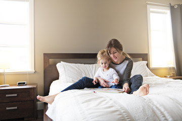 Fototapeta premium Cute little girl reading a book with her mother in the bedroom