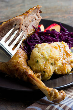 gebratene G&auml;nsekeule  mit Rotkohl und Kn&ouml;del auf einem Teller mit Besteck