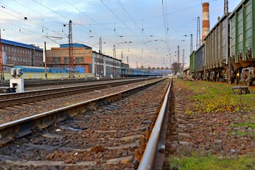 Naklejka na ściany i meble Railway station against beautiful sky at sunset. Industrial landscape with railroad, colorful cloudy blue sky. Railway sleepers. Railway junction. Heavy industry. Cargo shipping. Travel background