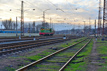 Obraz premium Railway station against beautiful sky at sunset. Industrial landscape with railroad, colorful cloudy blue sky. Railway sleepers. Railway junction. Heavy industry. Cargo shipping. Travel background