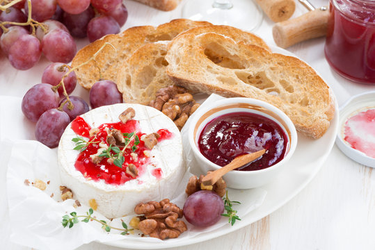 appetizers for wine - camembert with berry jam, toast and fruit on white table, top view