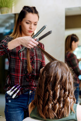 Working day inside the hair salon, hairdresser making hairstyle on young woman with hair straightener.