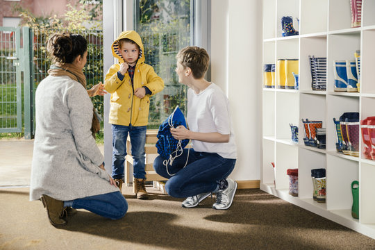 Boy in raincoat with mother and pre-school teacher in kindergarten