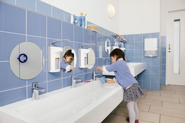 Little girl using water for brushing her teeth in bathroom of a kindergarten
