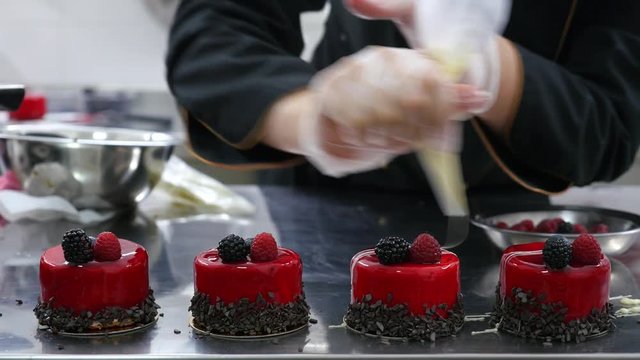 A confectioner decorating several mono portions with a cream...