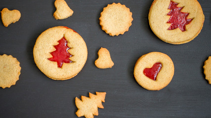 Ginger homemade cookies with strawberry jam on black wooden background with Christmas tree. Winter holidays concept. Flat lay, top view. Xmas Border - horizontal banner. Web size. 