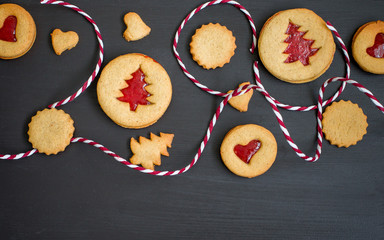 Ginger homemade cookies with strawberry jam on black wooden background with Christmas tree. Winter holidays concept. Flat lay, top view. Xmas Border - horizontal banner. Web size. 