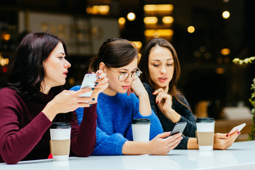 Three beautiful french girl friends using smartphone, chatting at cafe, modern lifestyle with gadget technology or working woman on freelance business concept.