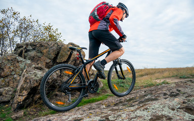 Fototapeta na wymiar Cyclist in Red Riding the Mountain Bike up Autumn Rocky Trail. Extreme Sport and Enduro Biking Concept.