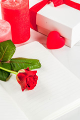 Holiday  background, Valentine's day. Bouquet of red roses, tie with a red ribbon, with blank notepad, wrapped gift box and red candle. On a white marble table, copy space