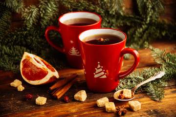 Obraz na płótnie Canvas Close-up two glass cups full of hot, red, aromatic lemon tea with dark chocolate on a pine branch and table background. Winter snacks composition.