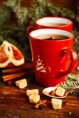 Close-up two glass cups full of hot, red, aromatic lemon tea with dark chocolate on a pine branch and table background. Winter snacks composition.