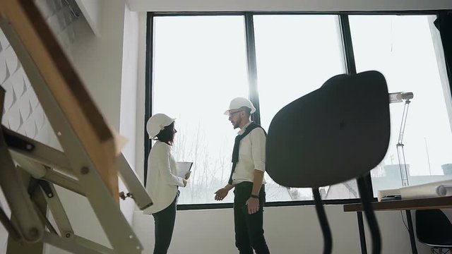 The architect and engineer stand at the big windows in the office and talk. Shared consent, handshakes