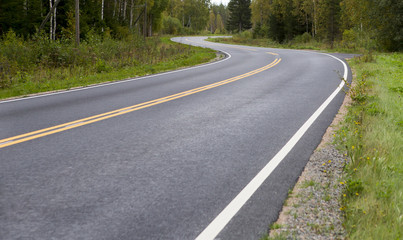 Curvy asphalt road on autumn day in Finland. Yellow lines and clean road. Highway to drive.
