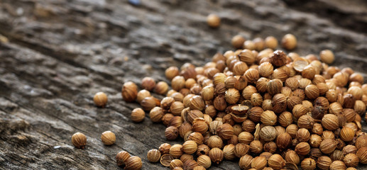 Dried coriander seeds in a pile set on old wooden surface.