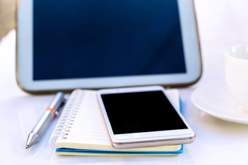 Tablet with a cup and smartphone on the white table.